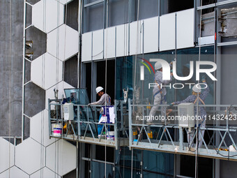 Workers are installing a glass curtain wall outside a high-rise building in Huai'an, China, on July 25, 2024. (