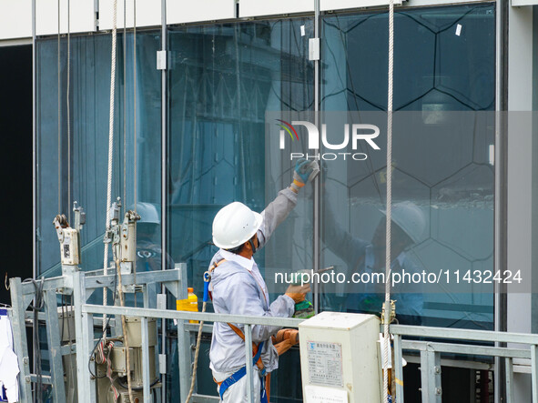 Workers are installing a glass curtain wall outside a high-rise building in Huai'an, China, on July 25, 2024. 