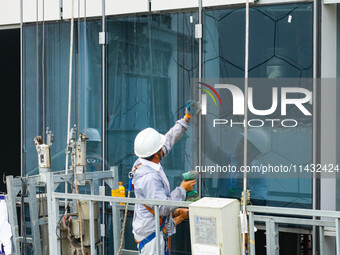 Workers are installing a glass curtain wall outside a high-rise building in Huai'an, China, on July 25, 2024. (