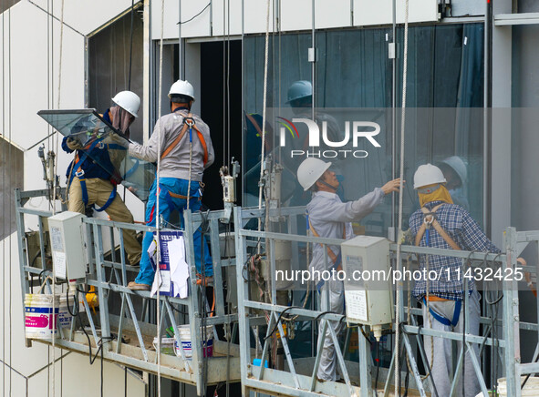 Workers are installing a glass curtain wall outside a high-rise building in Huai'an, China, on July 25, 2024. 