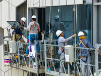 Workers are installing a glass curtain wall outside a high-rise building in Huai'an, China, on July 25, 2024. (