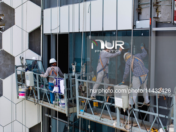 Workers are installing a glass curtain wall outside a high-rise building in Huai'an, China, on July 25, 2024. 