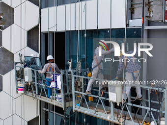 Workers are installing a glass curtain wall outside a high-rise building in Huai'an, China, on July 25, 2024. (