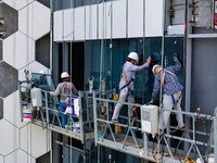 Workers are installing a glass curtain wall outside a high-rise building in Huai'an, China, on July 25, 2024. (