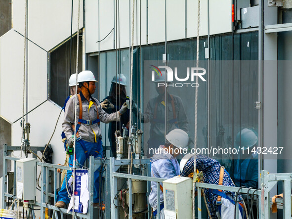 Workers are installing a glass curtain wall outside a high-rise building in Huai'an, China, on July 25, 2024. 