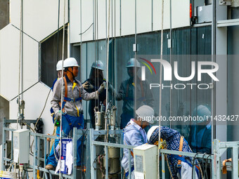 Workers are installing a glass curtain wall outside a high-rise building in Huai'an, China, on July 25, 2024. (