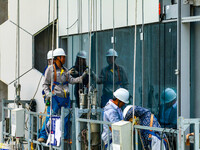 Workers are installing a glass curtain wall outside a high-rise building in Huai'an, China, on July 25, 2024. (