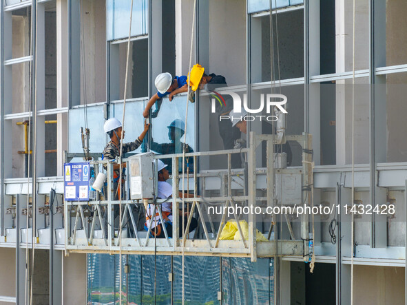 Workers are installing a glass curtain wall outside a high-rise building in Huai'an, China, on July 25, 2024. 