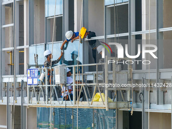 Workers are installing a glass curtain wall outside a high-rise building in Huai'an, China, on July 25, 2024. (