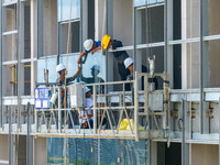 Workers are installing a glass curtain wall outside a high-rise building in Huai'an, China, on July 25, 2024. (