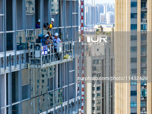 Workers are installing a glass curtain wall outside a high-rise building in Huai'an, China, on July 25, 2024. 