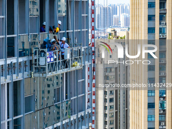 Workers are installing a glass curtain wall outside a high-rise building in Huai'an, China, on July 25, 2024. (