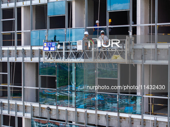 Workers are installing a glass curtain wall outside a high-rise building in Huai'an, China, on July 25, 2024. 