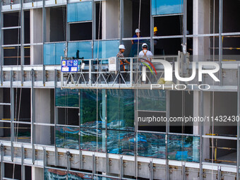 Workers are installing a glass curtain wall outside a high-rise building in Huai'an, China, on July 25, 2024. (