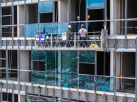 Workers are installing a glass curtain wall outside a high-rise building in Huai'an, China, on July 25, 2024. (