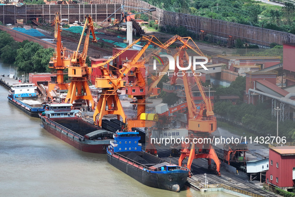 Cranes are unloading coal from a cargo ship on the Yangtze River at the raw material terminal of Meishan Iron and Steel Plant in Nanjing, Ch...