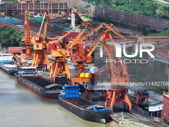 Cranes are unloading coal from a cargo ship on the Yangtze River at the raw material terminal of Meishan Iron and Steel Plant in Nanjing, Ch...