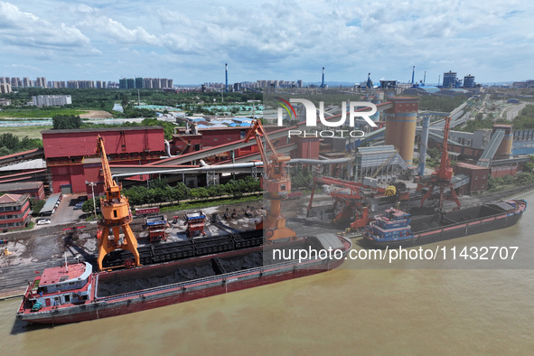 Cranes are unloading coal from a cargo ship on the Yangtze River at the raw material terminal of Meishan Iron and Steel Plant in Nanjing, Ch...