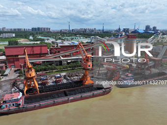 Cranes are unloading coal from a cargo ship on the Yangtze River at the raw material terminal of Meishan Iron and Steel Plant in Nanjing, Ch...