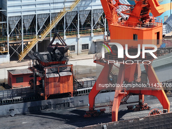 Cranes are unloading coal from a cargo ship on the Yangtze River at the raw material terminal of Meishan Iron and Steel Plant in Nanjing, Ch...