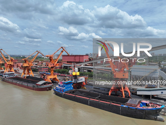 Cranes are unloading coal from a cargo ship on the Yangtze River at the raw material terminal of Meishan Iron and Steel Plant in Nanjing, Ch...