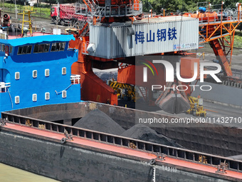 Cranes are unloading coal from a cargo ship on the Yangtze River at the raw material terminal of Meishan Iron and Steel Plant in Nanjing, Ch...