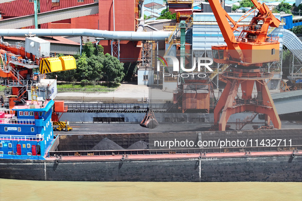 Cranes are unloading coal from a cargo ship on the Yangtze River at the raw material terminal of Meishan Iron and Steel Plant in Nanjing, Ch...