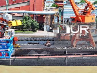 Cranes are unloading coal from a cargo ship on the Yangtze River at the raw material terminal of Meishan Iron and Steel Plant in Nanjing, Ch...