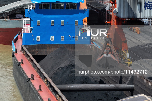 Cranes are unloading coal from a cargo ship on the Yangtze River at the raw material terminal of Meishan Iron and Steel Plant in Nanjing, Ch...