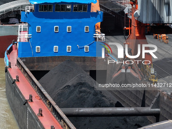 Cranes are unloading coal from a cargo ship on the Yangtze River at the raw material terminal of Meishan Iron and Steel Plant in Nanjing, Ch...