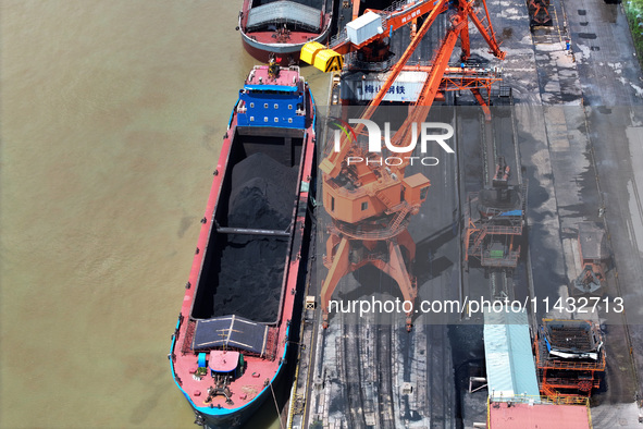 Cranes are unloading coal from a cargo ship on the Yangtze River at the raw material terminal of Meishan Iron and Steel Plant in Nanjing, Ch...