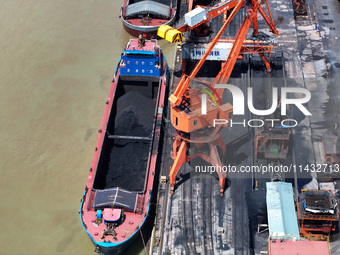 Cranes are unloading coal from a cargo ship on the Yangtze River at the raw material terminal of Meishan Iron and Steel Plant in Nanjing, Ch...