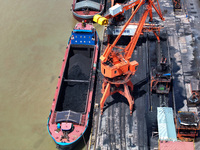 Cranes are unloading coal from a cargo ship on the Yangtze River at the raw material terminal of Meishan Iron and Steel Plant in Nanjing, Ch...