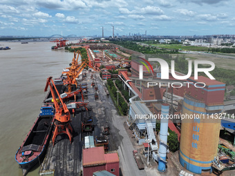 Cranes are unloading coal from a cargo ship on the Yangtze River at the raw material terminal of Meishan Iron and Steel Plant in Nanjing, Ch...