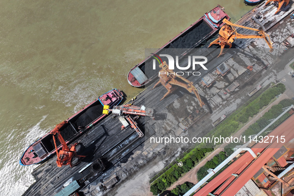 Cranes are unloading coal from a cargo ship on the Yangtze River at the raw material terminal of Meishan Iron and Steel Plant in Nanjing, Ch...