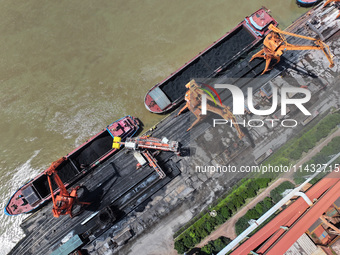 Cranes are unloading coal from a cargo ship on the Yangtze River at the raw material terminal of Meishan Iron and Steel Plant in Nanjing, Ch...