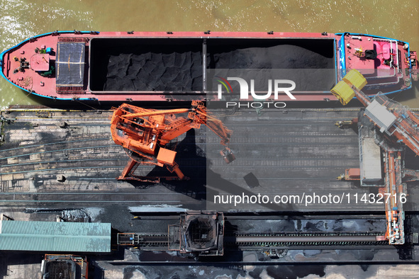 Cranes are unloading coal from a cargo ship on the Yangtze River at the raw material terminal of Meishan Iron and Steel Plant in Nanjing, Ch...