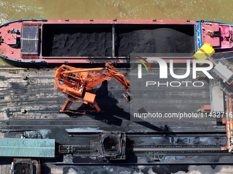 Cranes are unloading coal from a cargo ship on the Yangtze River at the raw material terminal of Meishan Iron and Steel Plant in Nanjing, Ch...