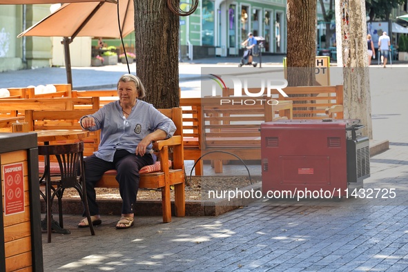 A woman is sitting at an outdoor cafe near a diesel generator used as a backup during power outages in Odesa, Ukraine, on July 23, 2024. NO...