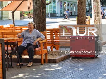 A woman is sitting at an outdoor cafe near a diesel generator used as a backup during power outages in Odesa, Ukraine, on July 23, 2024. NO...