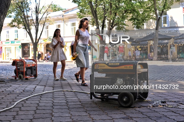 Women are walking past diesel generators in the street used as backups during power outages in Odesa, Ukraine, on July 23, 2024. NO USE RUSS...