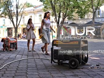 Women are walking past diesel generators in the street used as backups during power outages in Odesa, Ukraine, on July 23, 2024. NO USE RUSS...