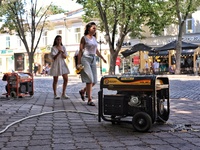 Women are walking past diesel generators in the street used as backups during power outages in Odesa, Ukraine, on July 23, 2024. NO USE RUSS...