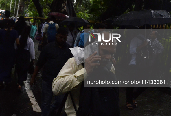 A man is talking on his phone covered with plastic material during rainfall in Mumbai, India, on July 25, 2024. 