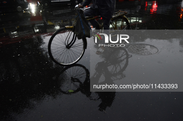 A reflection of a cyclist is being seen on a wet road during rainfall in Mumbai, India, on July 25, 2024. 