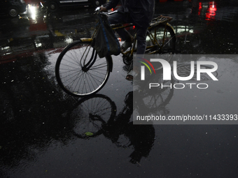 A reflection of a cyclist is being seen on a wet road during rainfall in Mumbai, India, on July 25, 2024. (