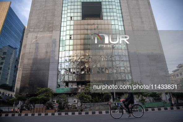 A cyclist is crossing past the burnt building of the Bangladesh Bridge Authority, which students are setting on fire amid the ongoing anti-q...