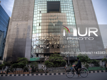 A cyclist is crossing past the burnt building of the Bangladesh Bridge Authority, which students are setting on fire amid the ongoing anti-q...