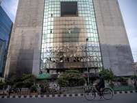 A cyclist is crossing past the burnt building of the Bangladesh Bridge Authority, which students are setting on fire amid the ongoing anti-q...