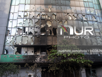 A cyclist is crossing past the burnt building of the Bangladesh Bridge Authority, which students are setting on fire amid the ongoing anti-q...